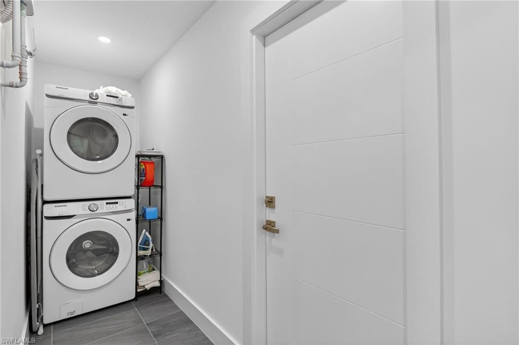 Washroom with stacked washer and clothes dryer and dark tile patterned floors