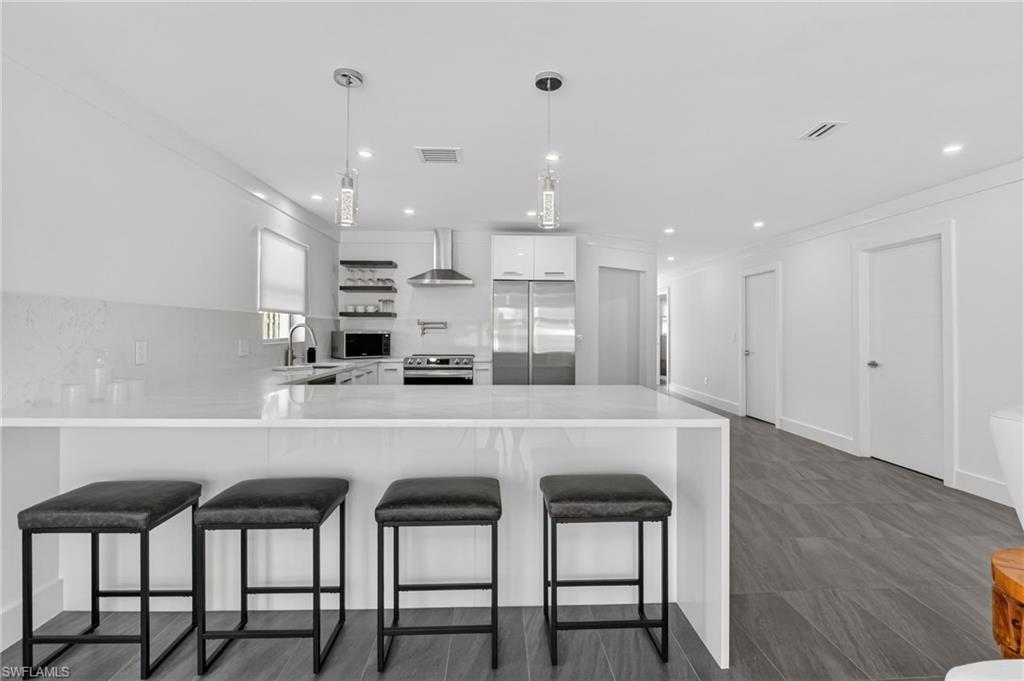Kitchen featuring a peninsula, appliances with stainless steel finishes, light stone counters, wall chimney range hood, and open shelves