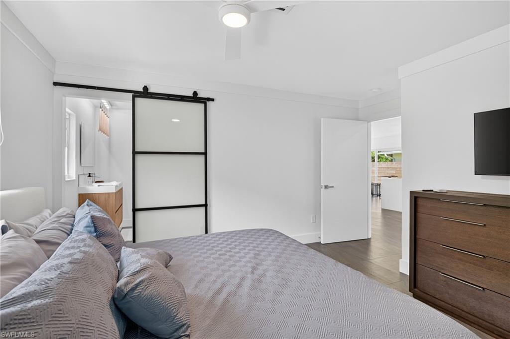 Bedroom with a barn door, a ceiling fan, and dark wood-style flooring