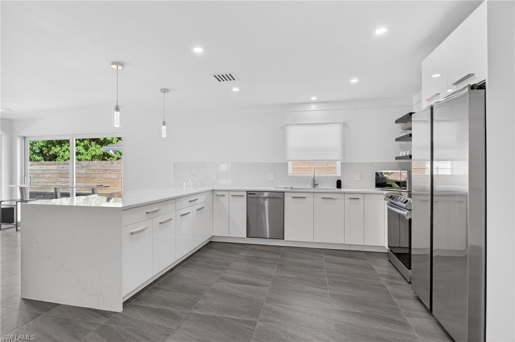 Kitchen with white cabinets, appliances with stainless steel finishes, pendant lighting, light stone countertops, and healthy amount of natural light