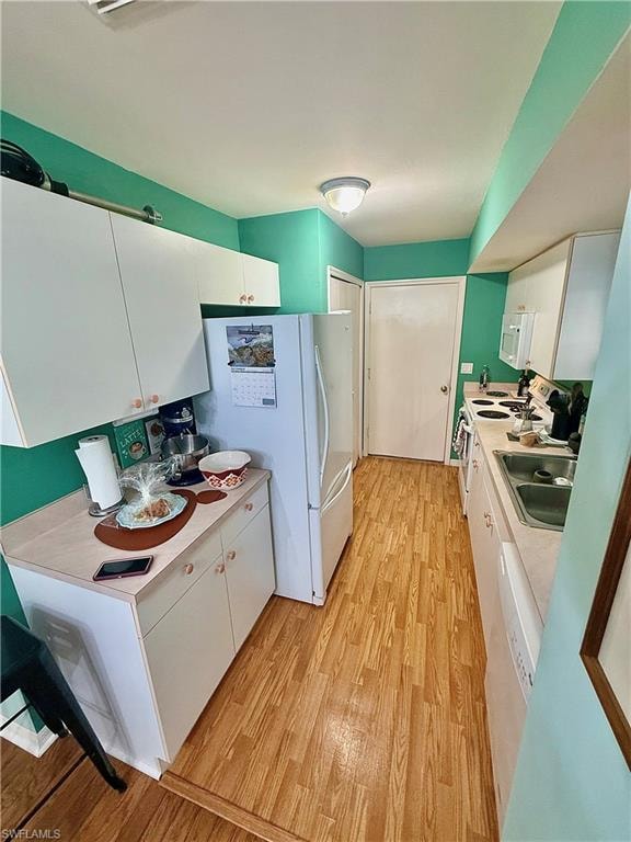 Kitchen with white cabinets, light countertops, white appliances, and light wood-style flooring