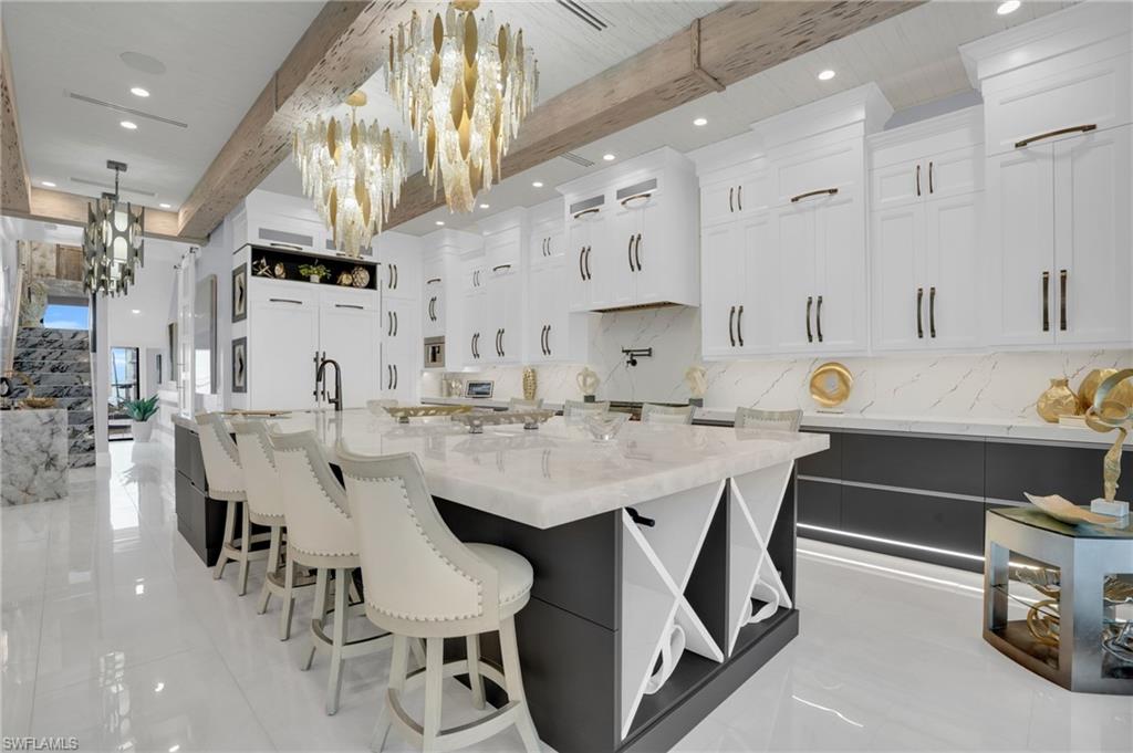 Kitchen with open shelves, white cabinets, light stone counters, beam ceiling, and decorative light fixtures - Virtually Edited Image