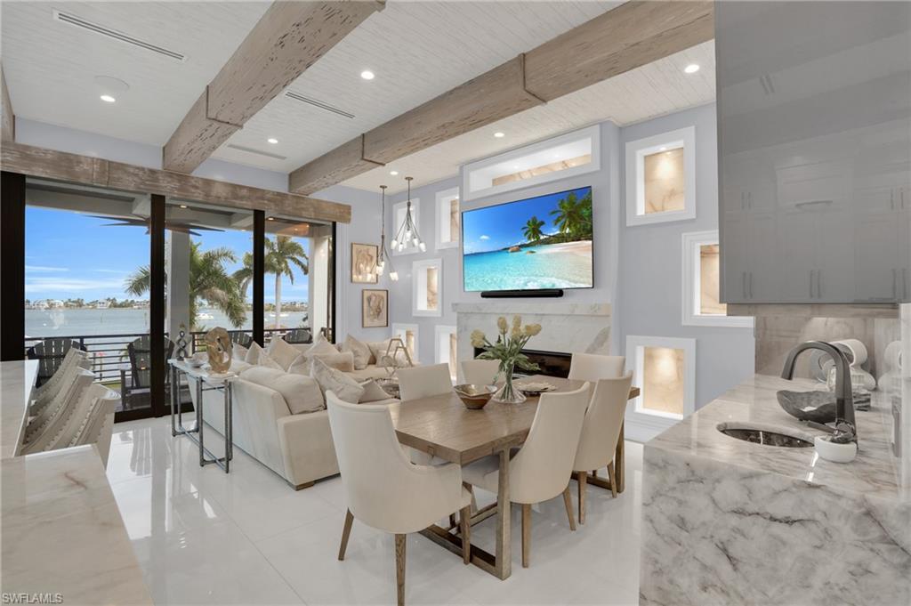Dining area featuring a glass covered fireplace, beamed ceiling, recessed lighting, a water view, and light tile patterned floors - Virtually Edited Image