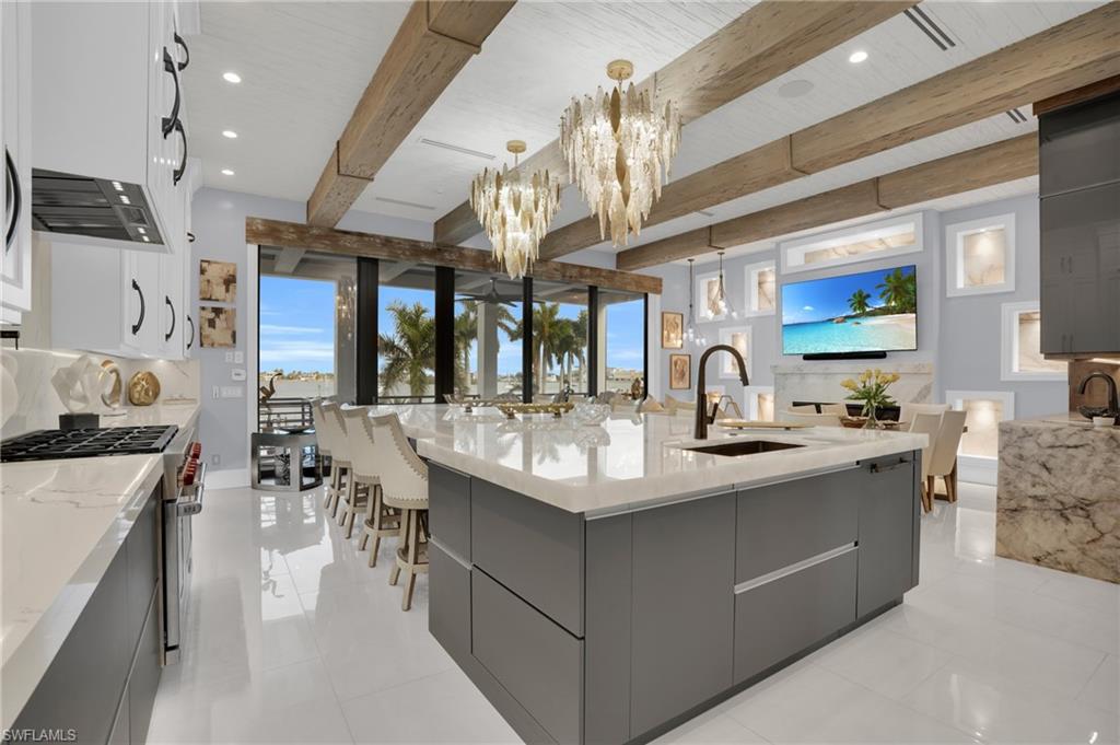 Kitchen with modern cabinets, a large island with sink, light stone countertops, beam ceiling, and recessed lighting - Virtually Edited Image