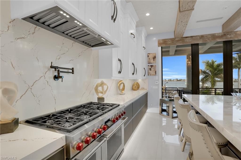 Kitchen with premium range hood, range with two ovens, decorative backsplash, white cabinetry, and beamed ceiling - Virtually Edited Image
