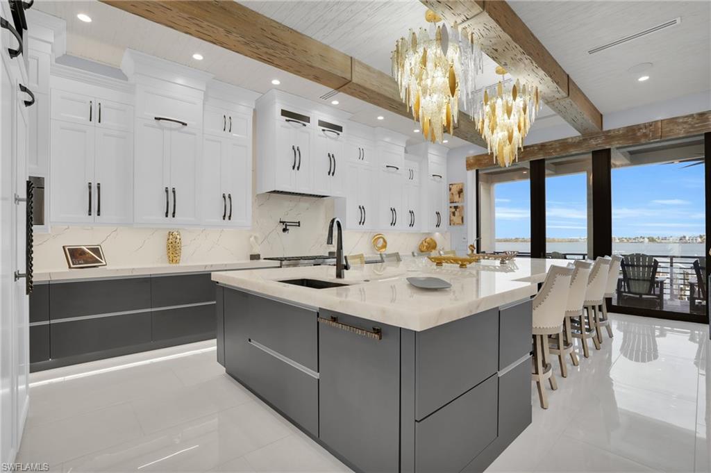 Kitchen with beamed ceiling, white cabinets, a spacious island, gray cabinets, and pendant lighting - Virtually Edited Image