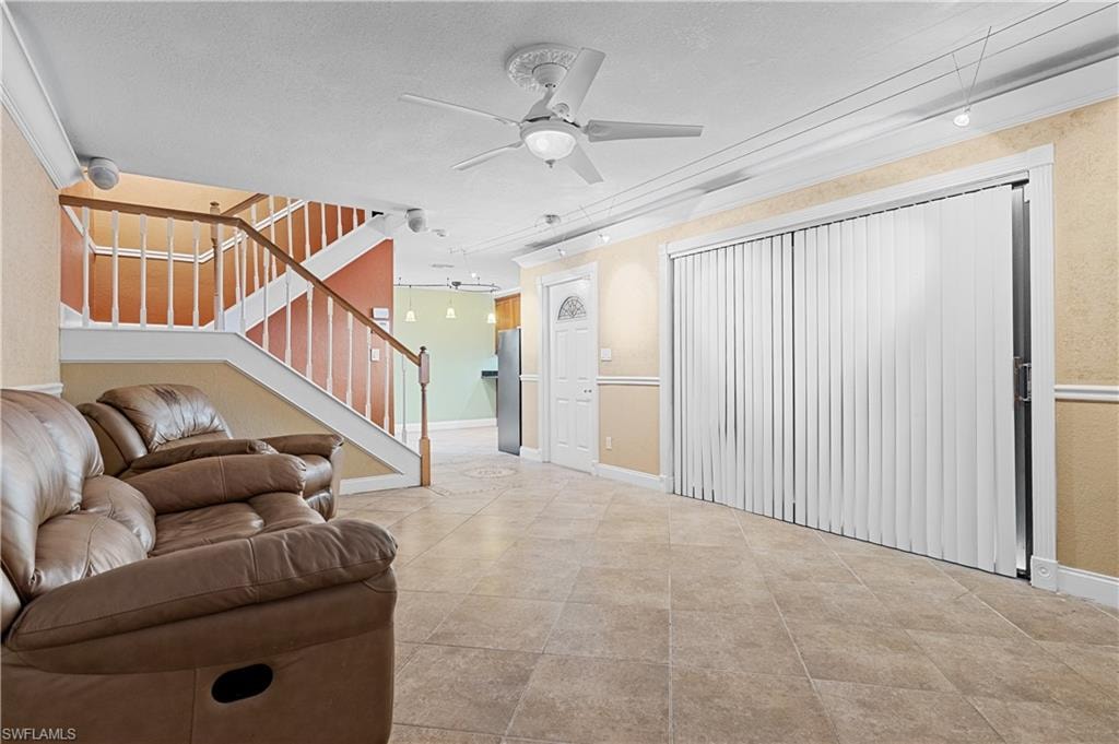 Living room with a ceiling fan, a textured ceiling, and stairs