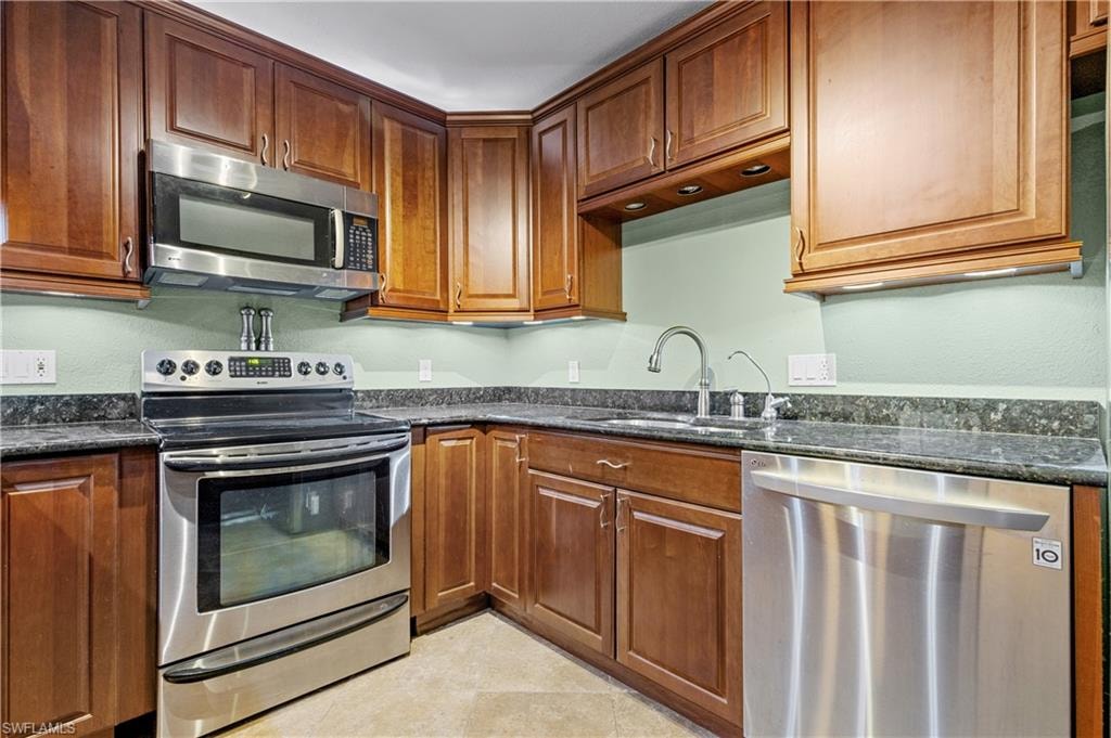 Kitchen with appliances with stainless steel finishes, dark stone countertops, and brown cabinets