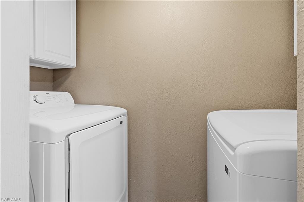 Laundry room featuring washer and clothes dryer, a textured wall, and cabinet space