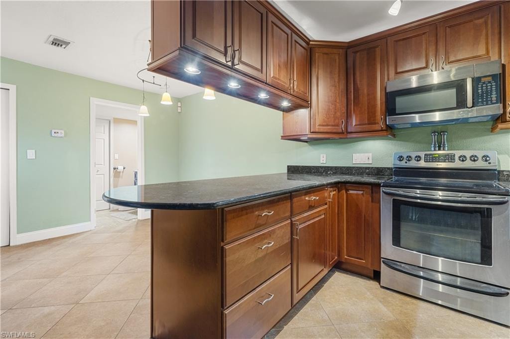 Kitchen featuring appliances with stainless steel finishes, a peninsula, light tile patterned flooring, and dark stone countertops