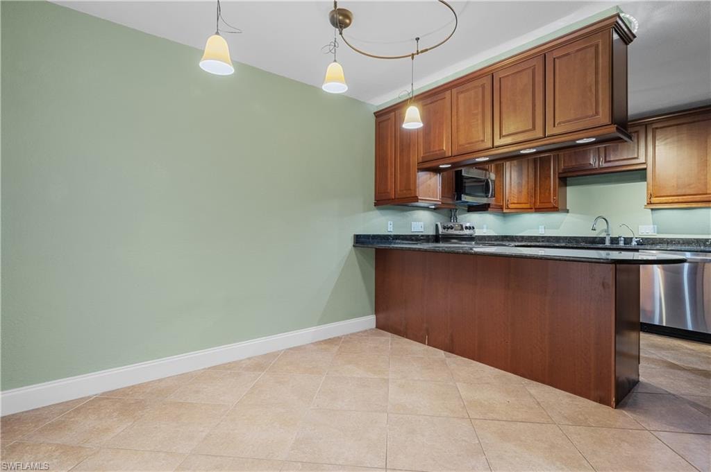 Kitchen with brown cabinetry, pendant lighting, appliances with stainless steel finishes, and dark stone countertops