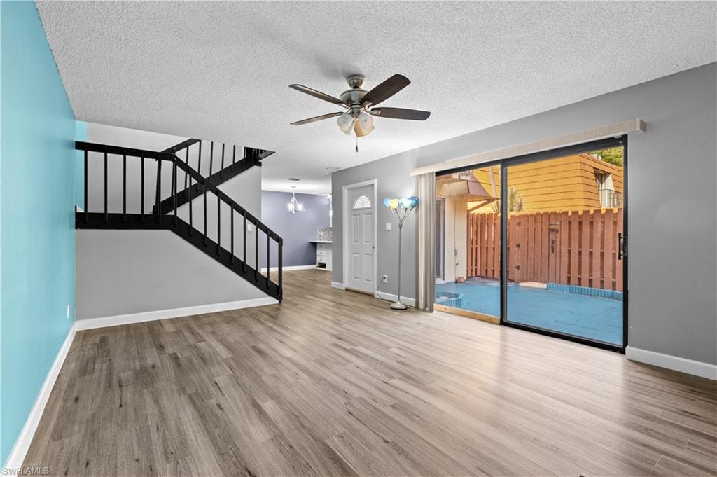 Unfurnished living room featuring stairs, light wood-style flooring, a textured ceiling, ceiling fan, and a chandelier
