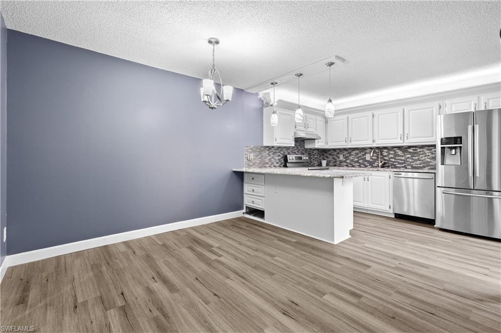 Kitchen with white cabinetry, stainless steel appliances, pendant lighting, a peninsula, and a textured ceiling