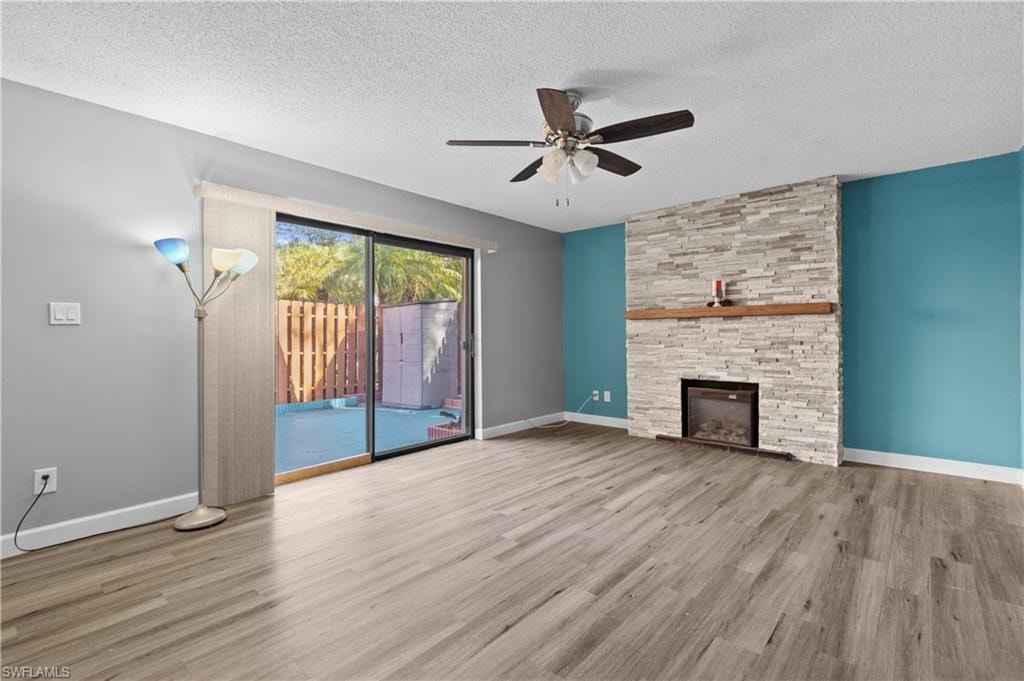 Unfurnished living room featuring light wood-style flooring, a stone fireplace, ceiling fan, and a textured ceiling