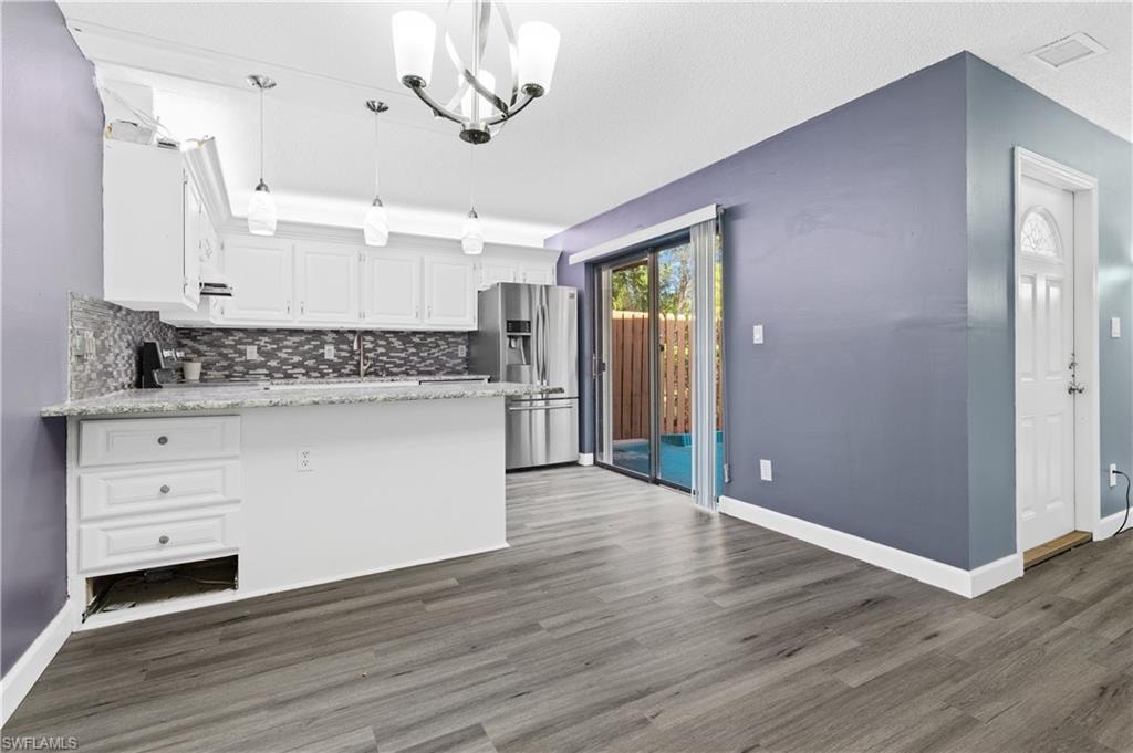Kitchen with a peninsula, white cabinetry, pendant lighting, light stone countertops, and stainless steel refrigerator with ice dispenser