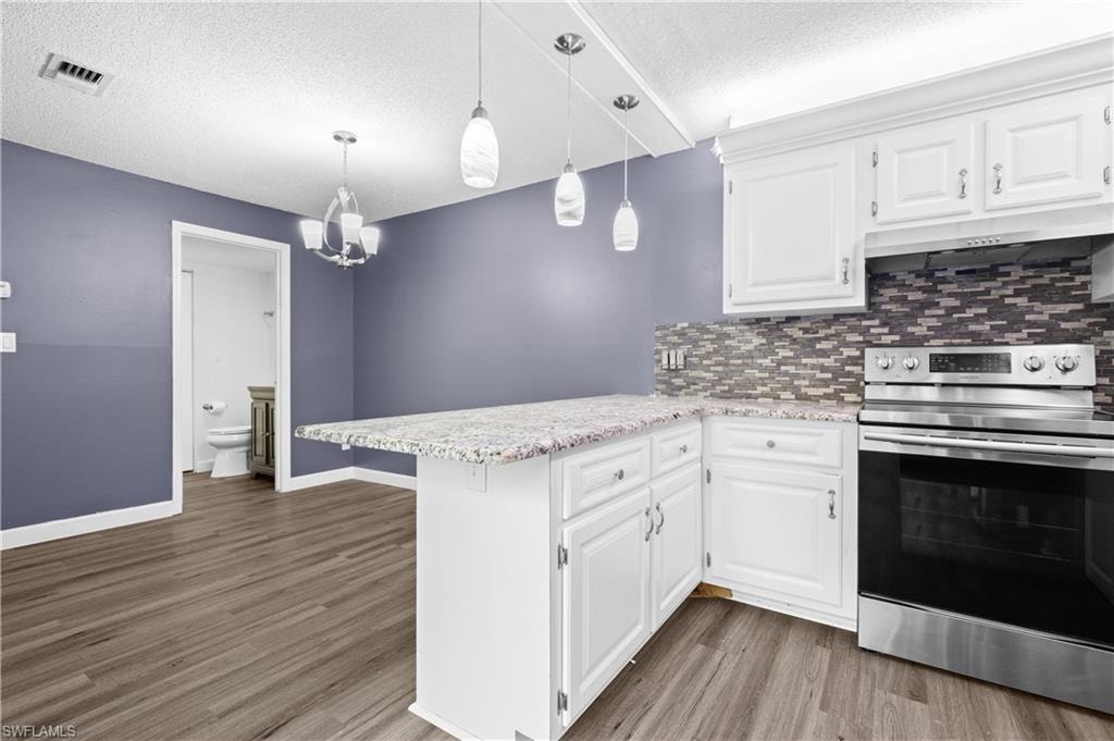 Kitchen featuring stainless steel range with electric stovetop, white cabinets, a peninsula, decorative backsplash, and a textured ceiling