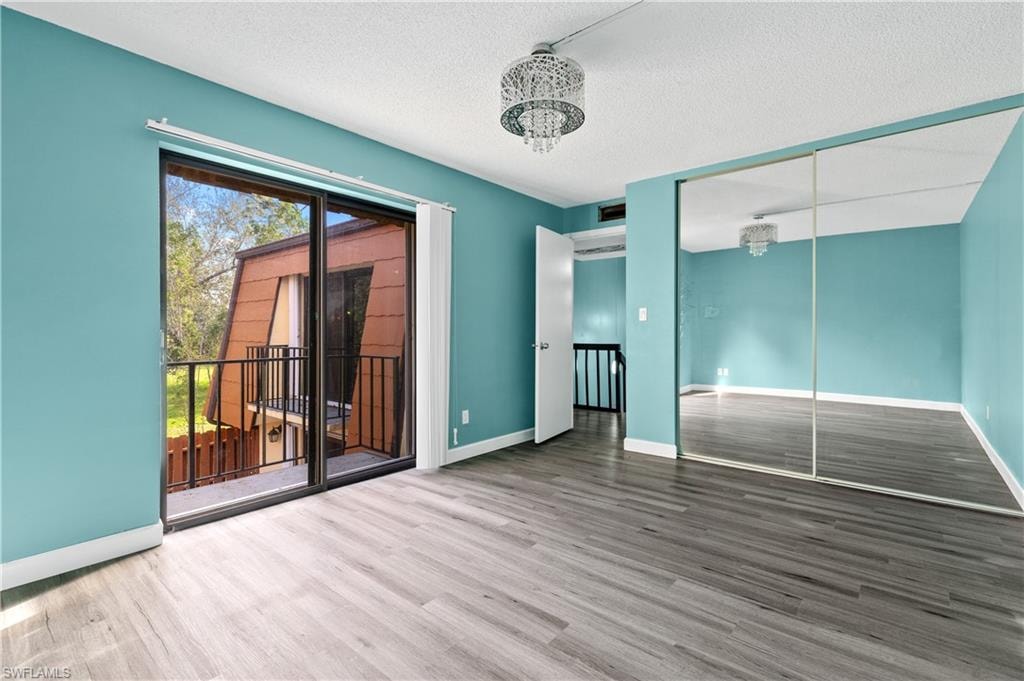 Unfurnished bedroom featuring a textured ceiling, wood finished floors, a closet, access to outside, and a chandelier