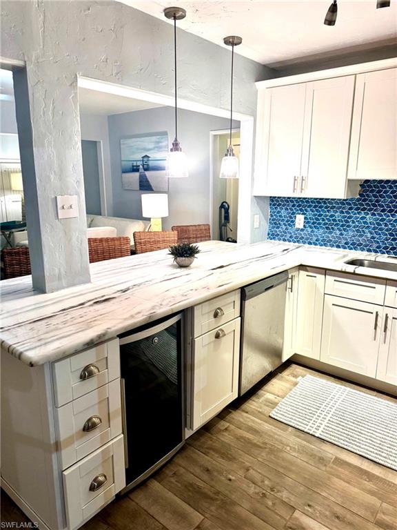 Kitchen with white cabinets, stainless steel dishwasher, wine cooler, dark wood-style flooring, and a textured wall