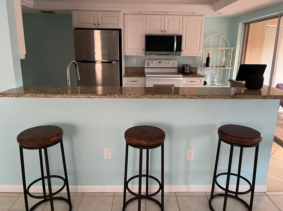 Kitchen featuring a kitchen breakfast bar, white cabinetry, light tile patterned flooring, and stainless steel appliances