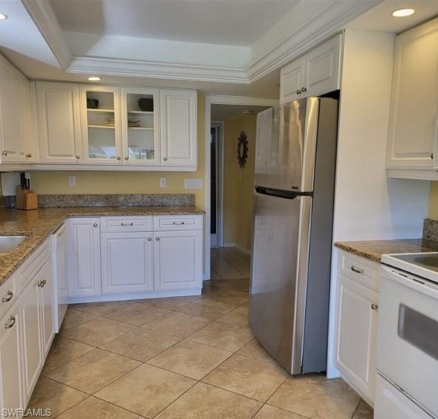 Kitchen with white cabinets, white appliances, a tray ceiling, and crown molding