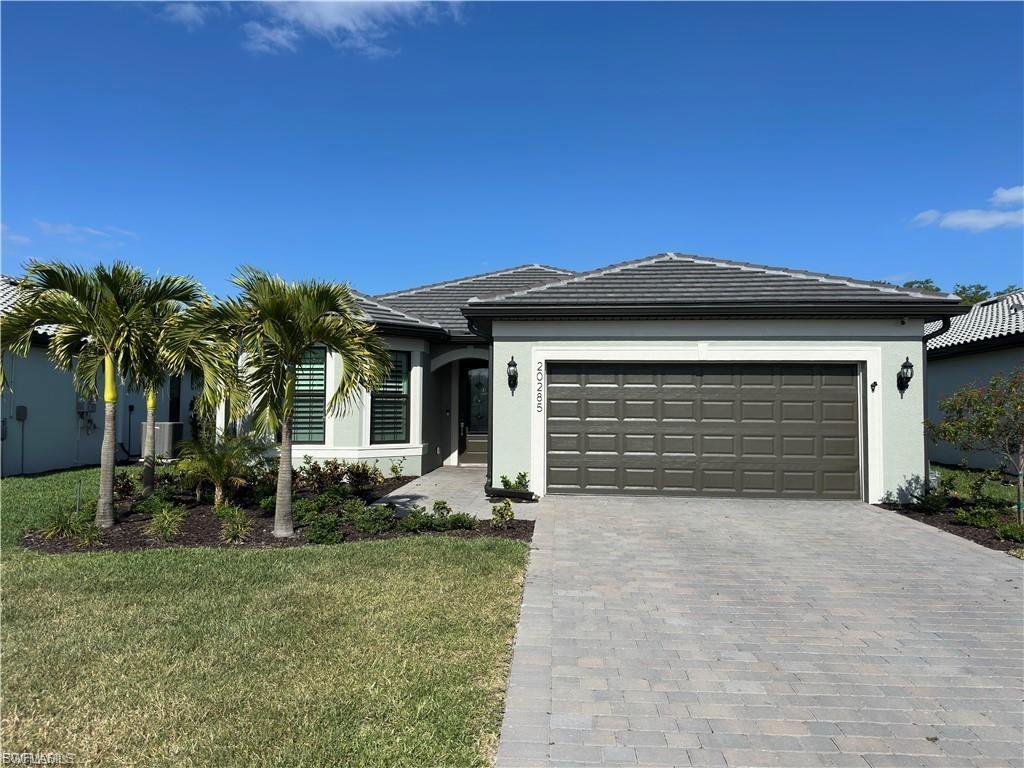 View of front of property with decorative driveway, a tile roof, stucco siding, and a front yard
