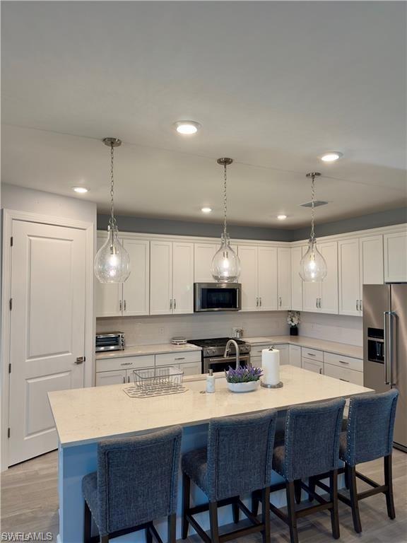 Kitchen with a kitchen bar, light wood-style floors, white cabinets, appliances with stainless steel finishes, and decorative light fixtures