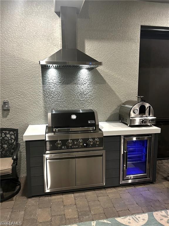 Kitchen with a textured wall, wall chimney range hood, light countertops, and beverage cooler