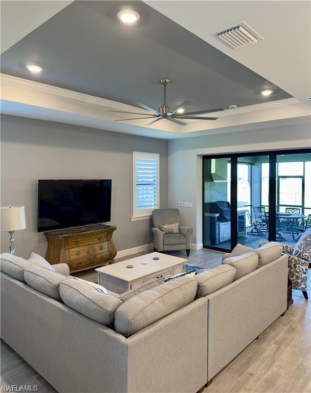 Living area featuring crown molding, a tray ceiling, light wood-type flooring, and recessed lighting