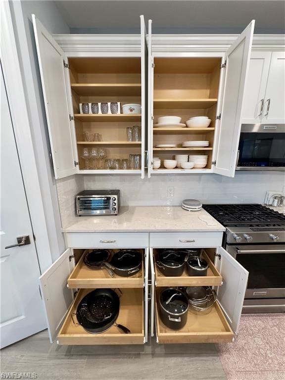 Kitchen view of appliances with stainless steel finishes, white cabinetry, light stone counters, and light wood finished floors