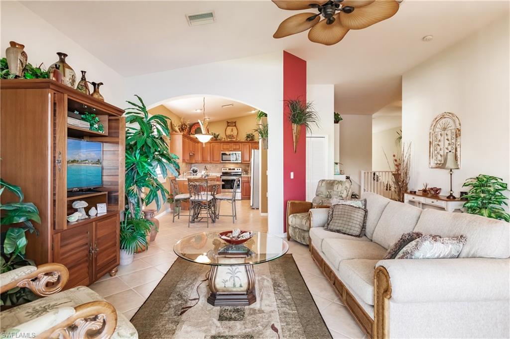 Living room with arched walkways, light tile patterned floors, lofted ceiling, and ceiling fan