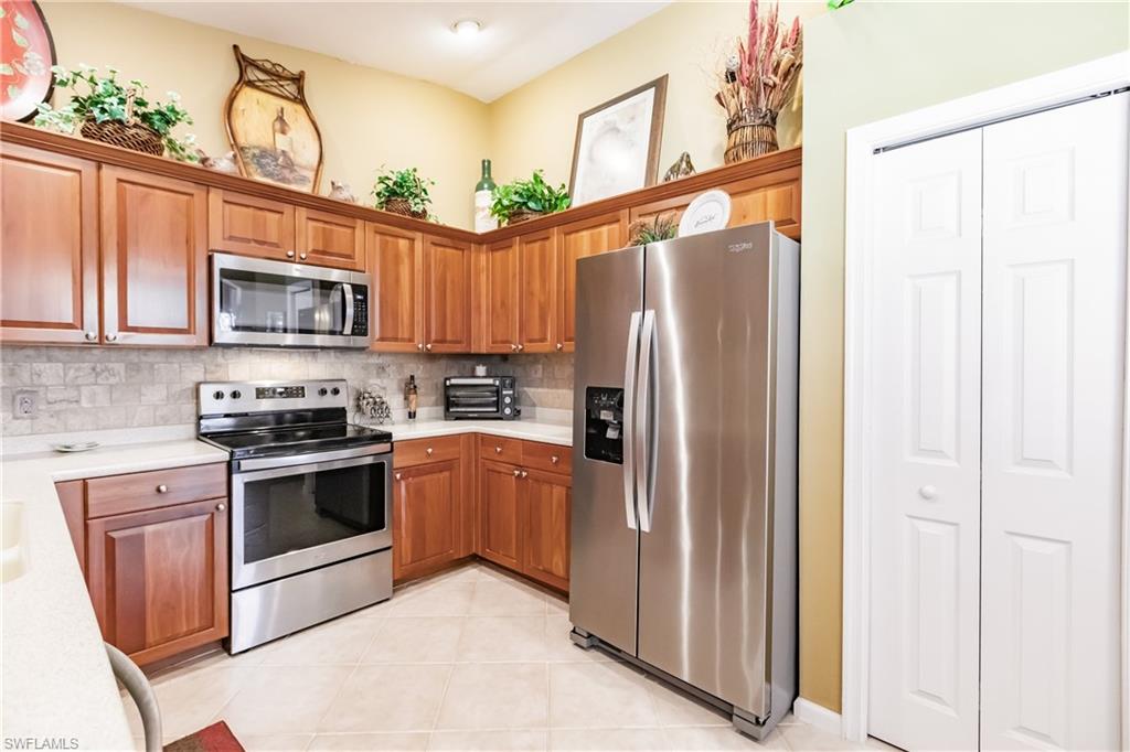 Kitchen with appliances with stainless steel finishes, brown cabinetry, backsplash, light tile patterned floors, and light stone counters