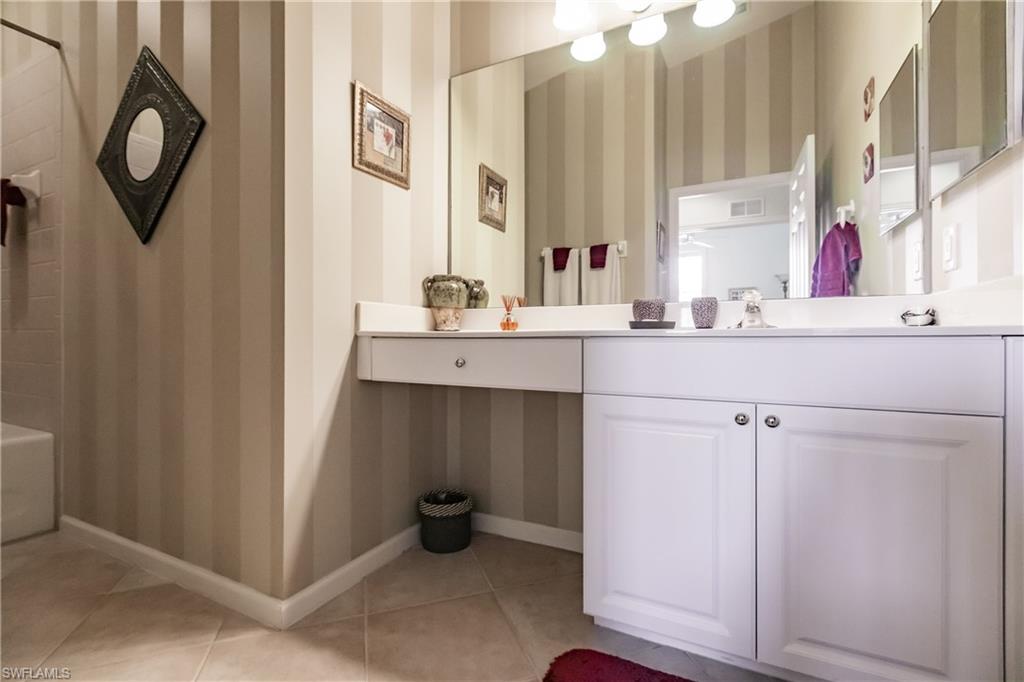 Bathroom with wallpapered walls, vanity,  shower combination, and light tile patterned floors