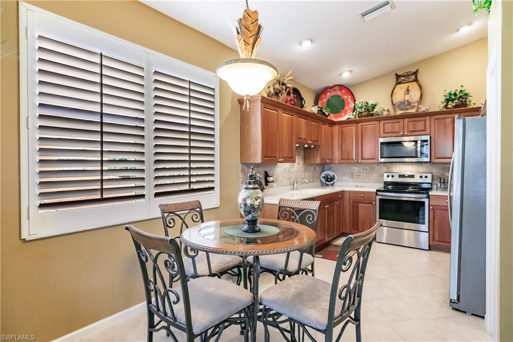 Kitchen featuring appliances with stainless steel finishes, light countertops, brown cabinetry, pendant lighting, and tasteful backsplash