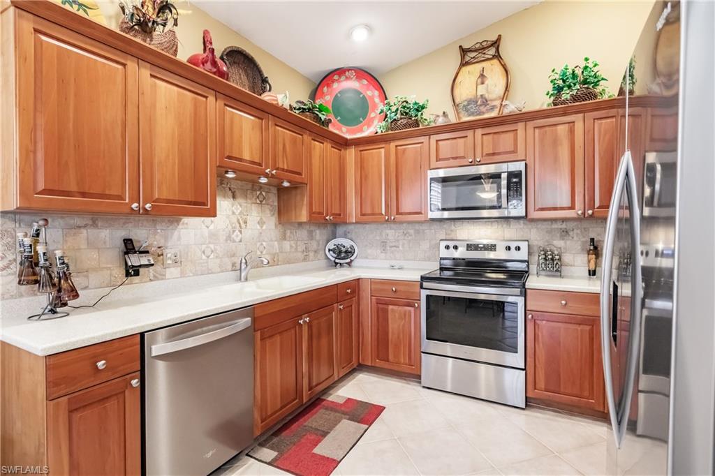 Kitchen featuring stainless steel appliances, brown cabinetry, light tile patterned floors, and light stone countertops