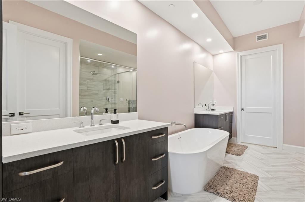 Bathroom with a stall shower, two vanities, a freestanding bath, and recessed lighting