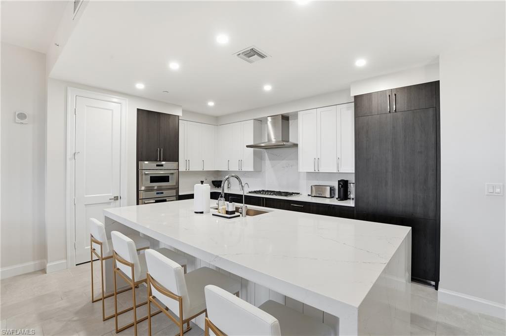 Kitchen featuring white cabinets, a kitchen bar, light stone countertops, a kitchen island with sink, and recessed lighting