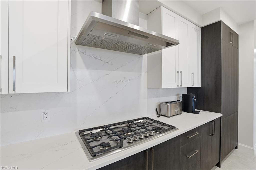 Kitchen featuring white cabinets, wall chimney exhaust hood, dark brown cabinetry, stainless steel gas stovetop, and light stone countertops