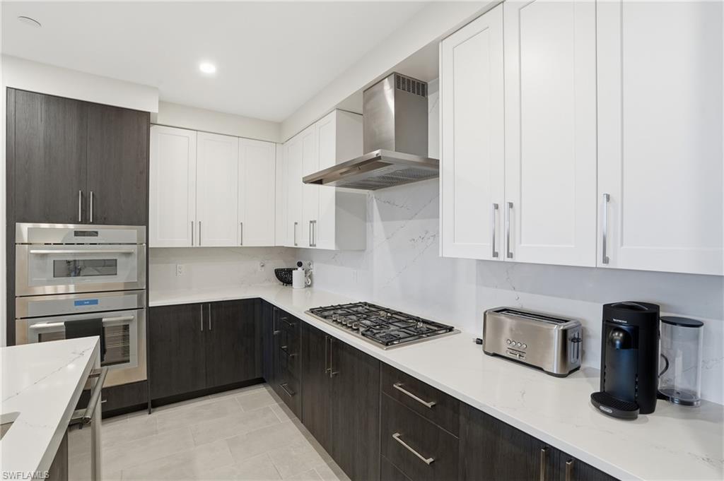 Kitchen featuring white cabinetry, light stone counters, wall chimney exhaust hood, and decorative backsplash