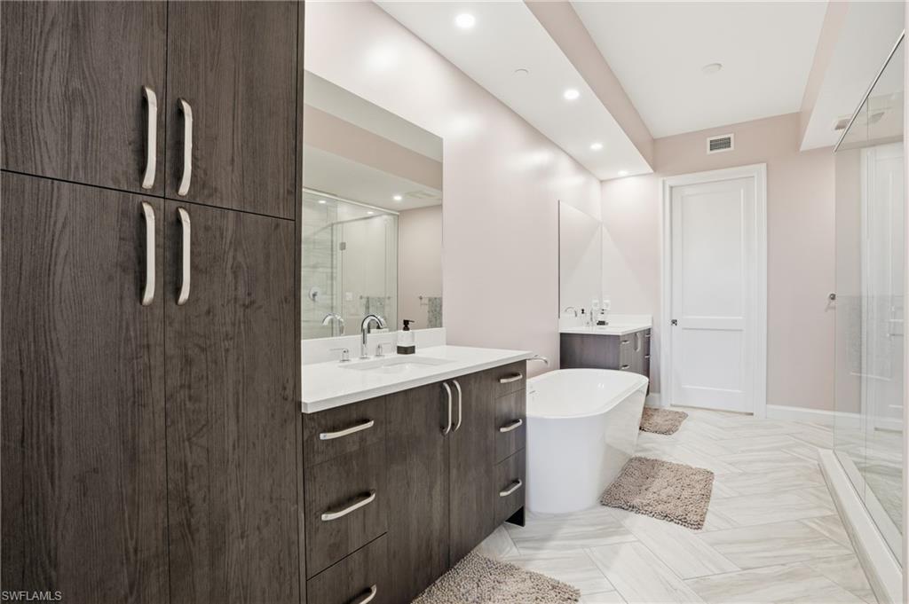 Full bathroom with two vanities, a stall shower, a freestanding tub, and recessed lighting
