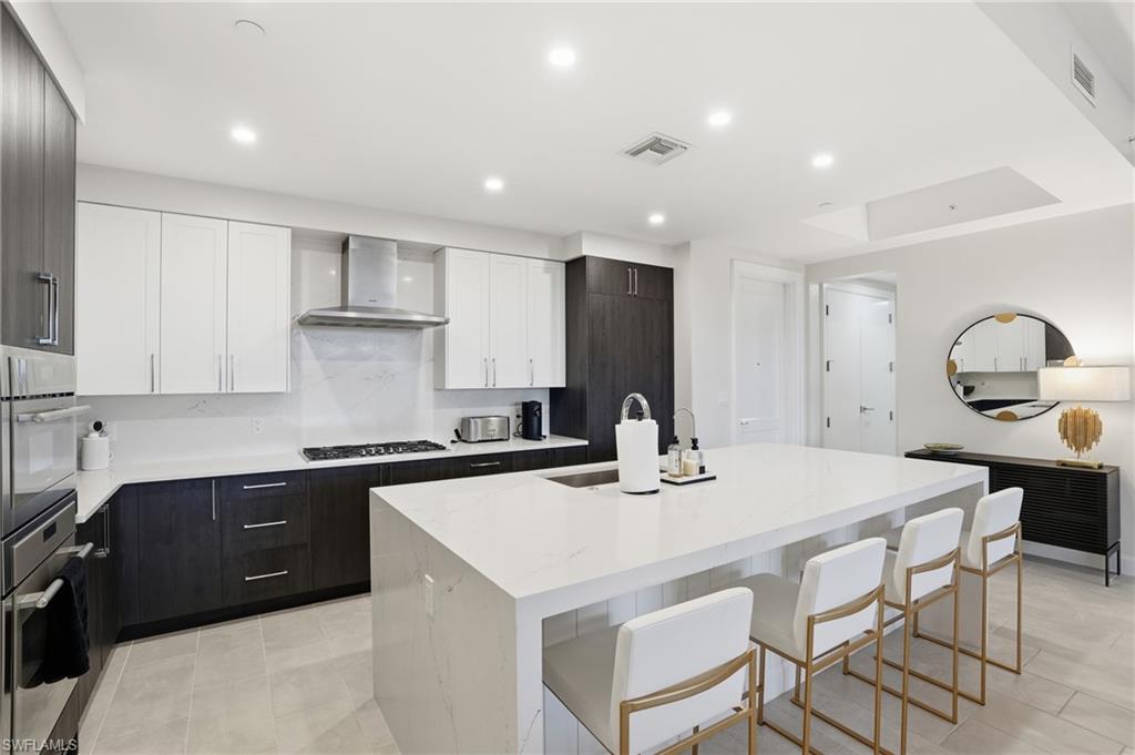 Kitchen with white cabinetry, an island with sink, light stone countertops, a kitchen breakfast bar, and stainless steel appliances