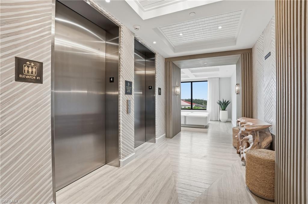 Hallway with a tray ceiling, elevator, and recessed lighting