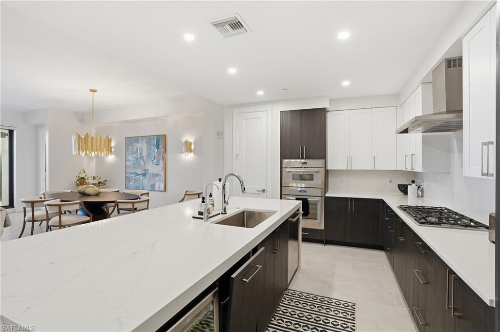 Kitchen with white cabinetry, pendant lighting, recessed lighting, wall chimney range hood, and light stone counters