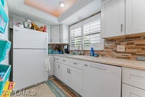 Kitchen with white appliances, white cabinets, a tray ceiling, light countertops, and crown molding