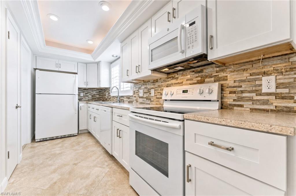 Kitchen featuring white cabinetry, light-toned countertops, and a stacked stone-look backsplash. Virtually removed clutter from counter tops etc.