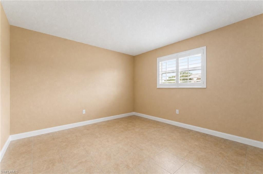 Spacious room featuring neutral wall tones, large format tile flooring, and a window with plantation shutters. Virtually removed furniture, lightened walls.