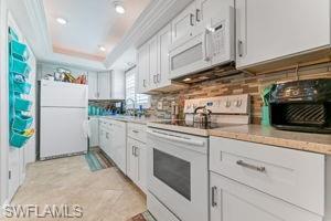 Kitchen with white appliances, white cabinetry, light countertops, a tray ceiling, and ornamental molding