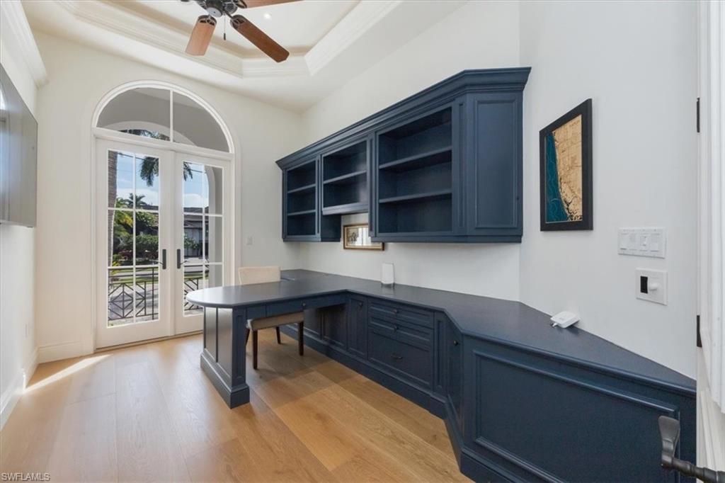 Home office with built in desk, french doors, a raised ceiling, light wood-style flooring, and ceiling fan