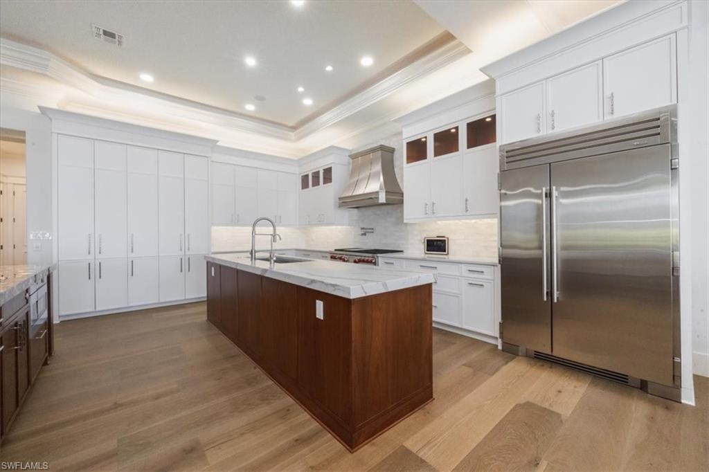 Kitchen with glass insert cabinets, appliances with stainless steel finishes, white cabinetry, a kitchen island with sink, and crown molding