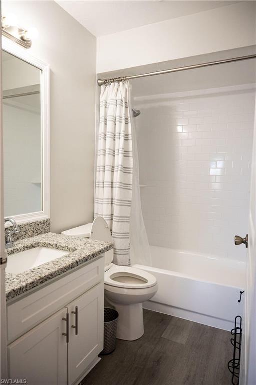 Full bath with vanity, shower / bath combo with shower curtain, and dark wood-type flooring