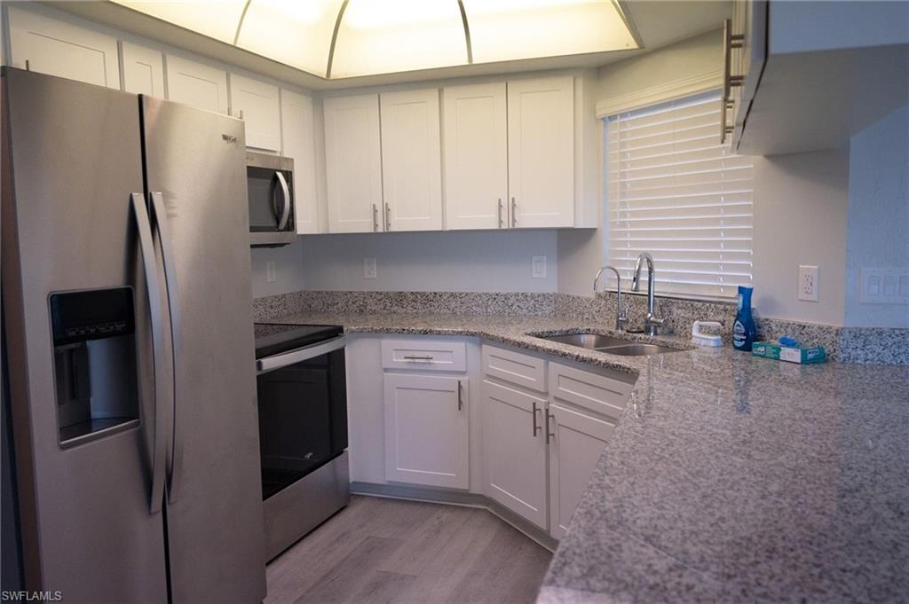 Kitchen with stainless steel appliances, light stone counters, white cabinetry, and light wood-style flooring